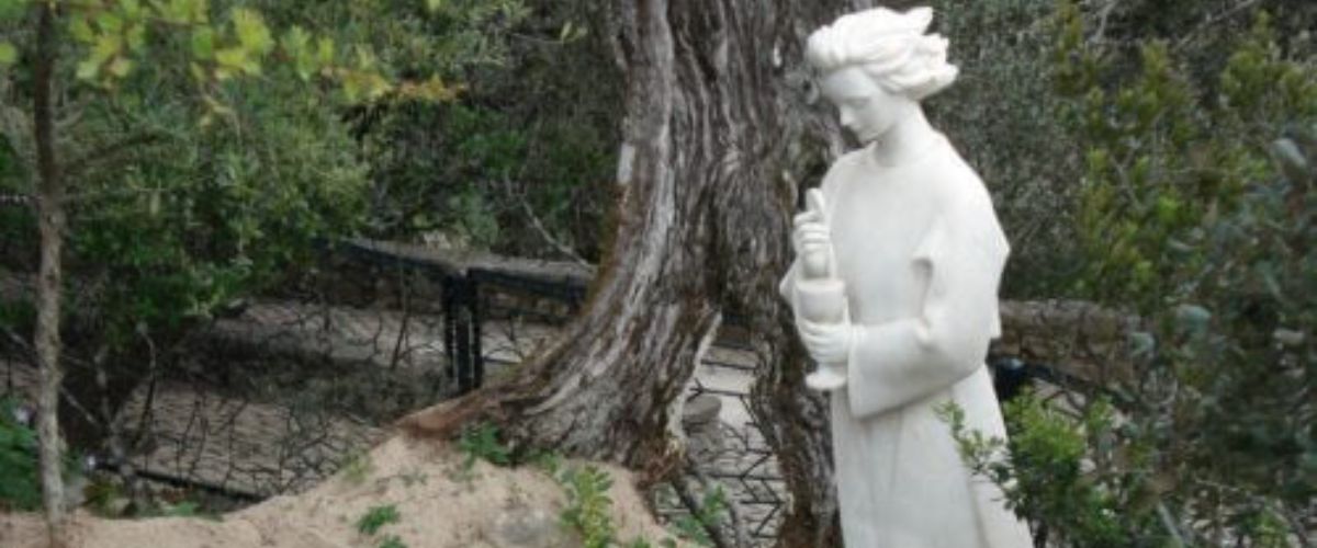 Statues of Blessed Jacinta and Francisco Marto kneeling in prayer before an angel in a garden setting.