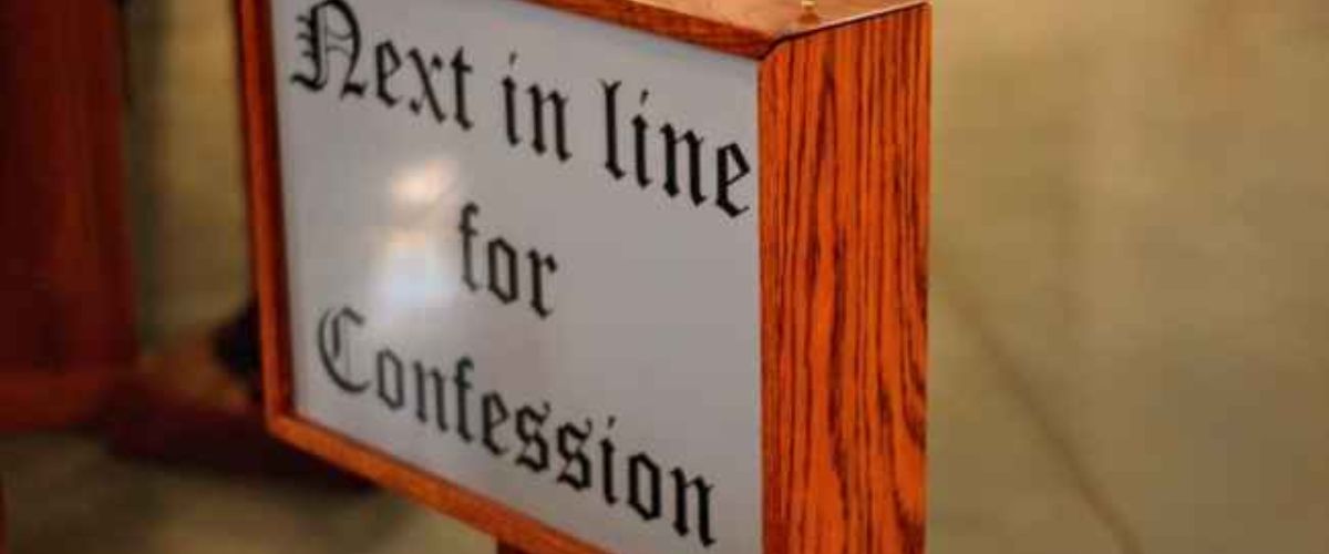 Wooden church sign reading “Next in line for Confession.”