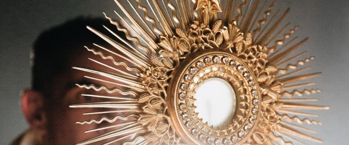 Golden Eucharistic monstrance with a host at the center, held during Catholic adoration.