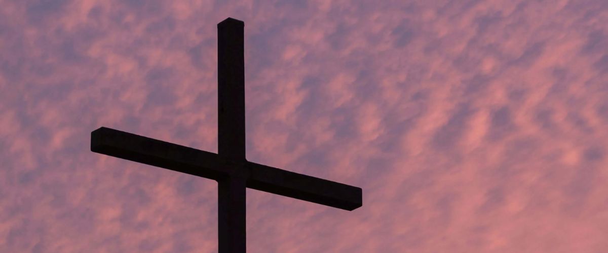 Silhouette of a cross against a pink and purple sunset sky