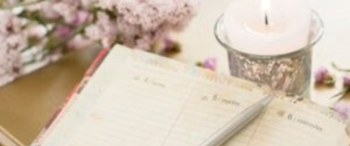 Open journal with a pen beside a lit candle and soft flowers, creating a calm and reflective setting