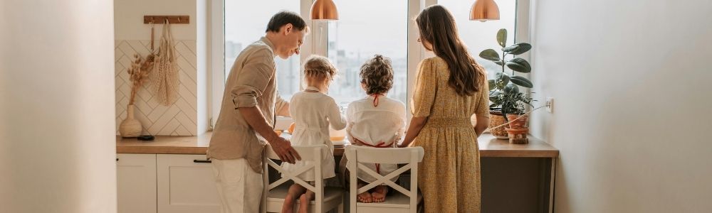 Parents and two young children standing together at a kitchen counter, sharing a quiet family moment in a bright, cozy home.