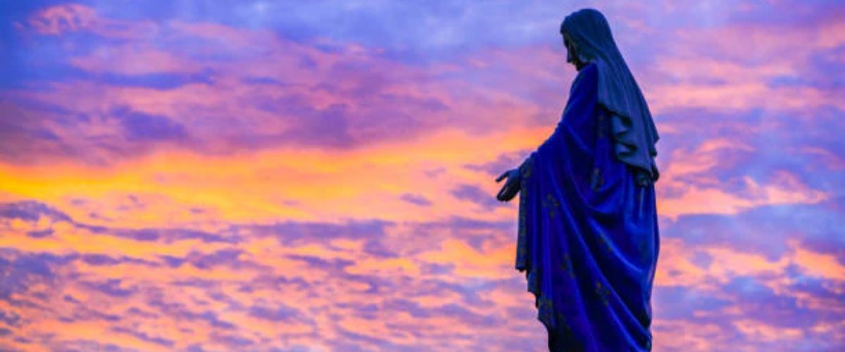 Silhouette of a statue of the Virgin Mary against a colorful sunset sky.
