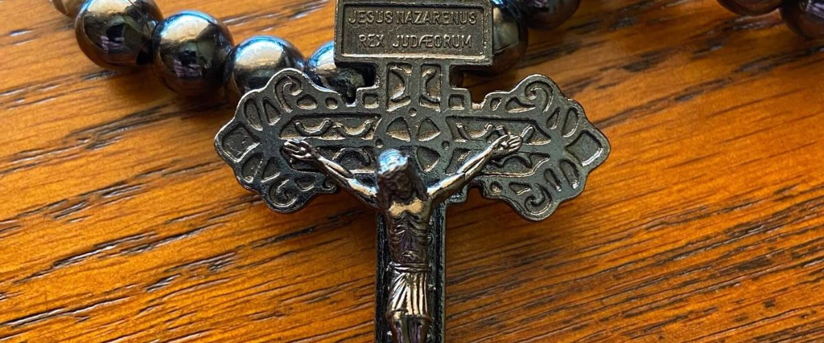 Black rosary beads with a metal crucifix featuring Jesus on the cross, resting on a wooden surface.