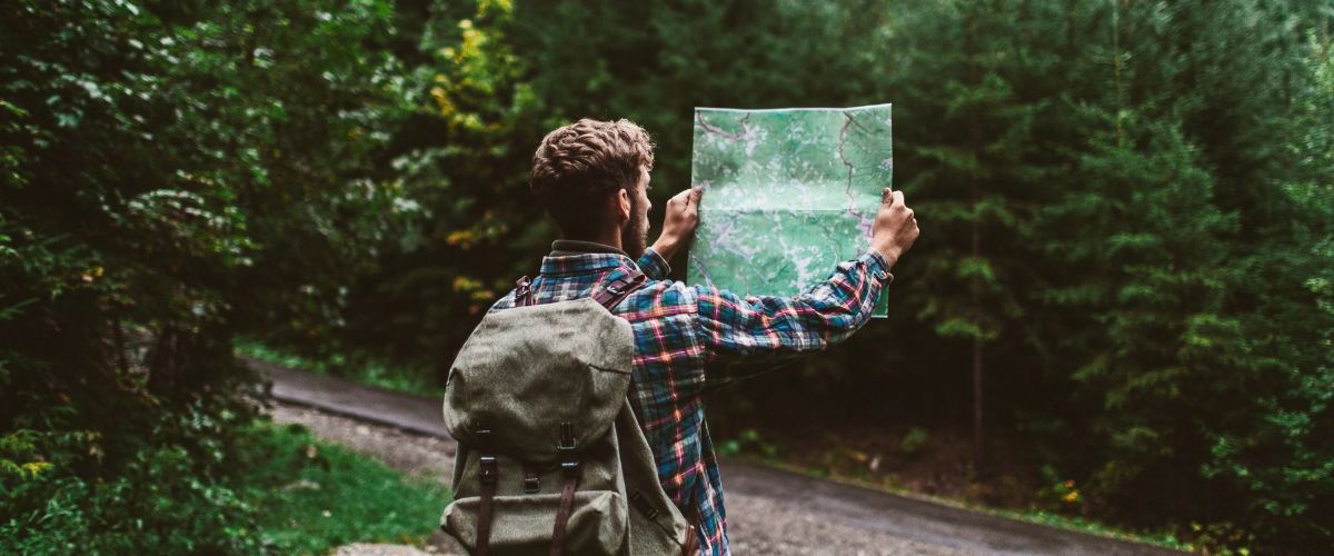 Person with a backpack holding a map while standing on a forest path