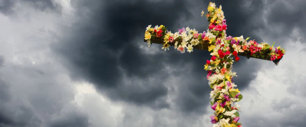 Flower-covered cross set against a dark, cloudy sky