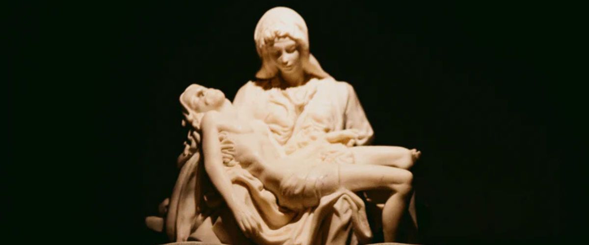 Statue of the Pietà showing Mary holding the body of Jesus above an open book.