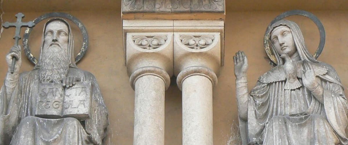 Stone statues of St. Benedict and St. Scholastica seated with halos on a church façade.