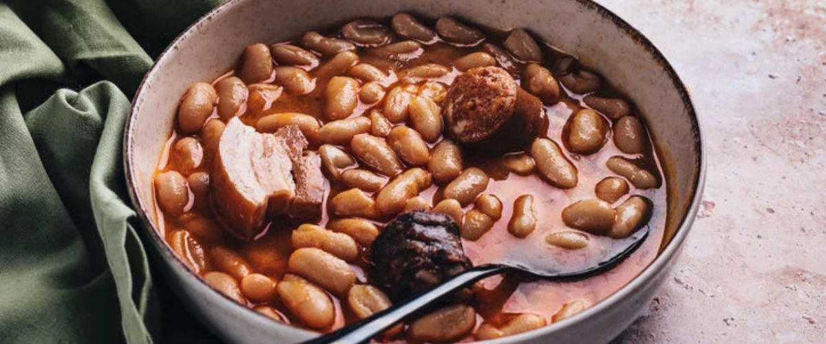 Bowl of stewed beans with sausage and chunks of meat in a rich broth