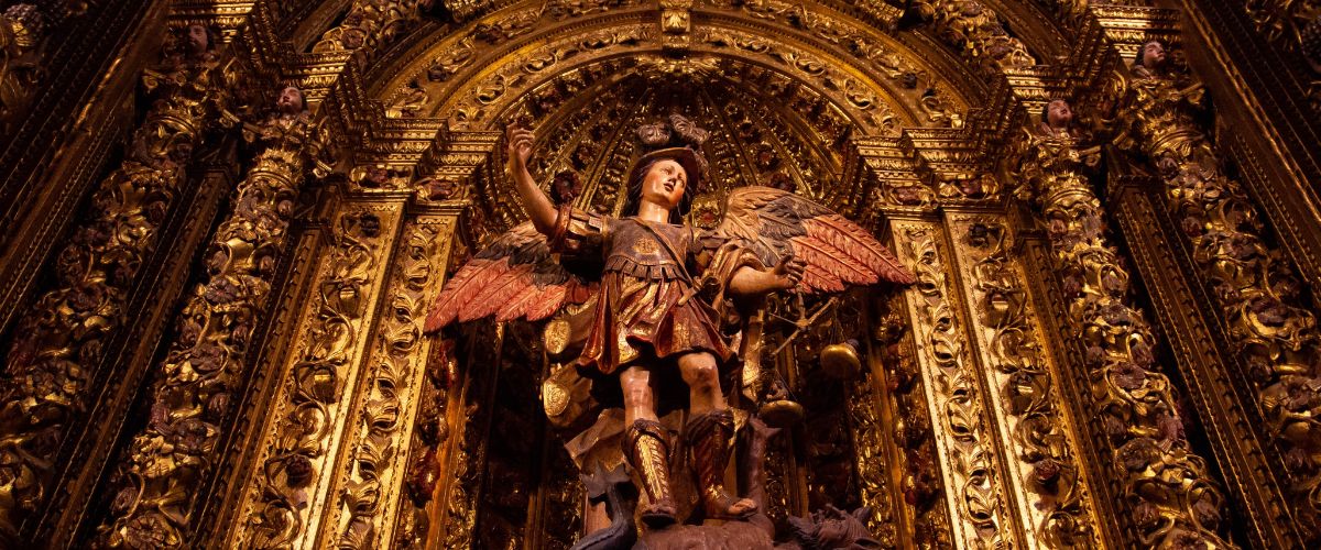 Statue of St. Michael the Archangel defeating a dragon beneath an ornate gold church altar