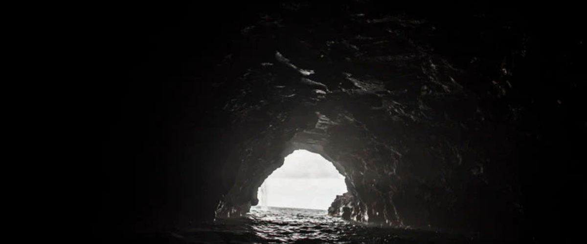Dark sea cave opening to the ocean with light shining through.