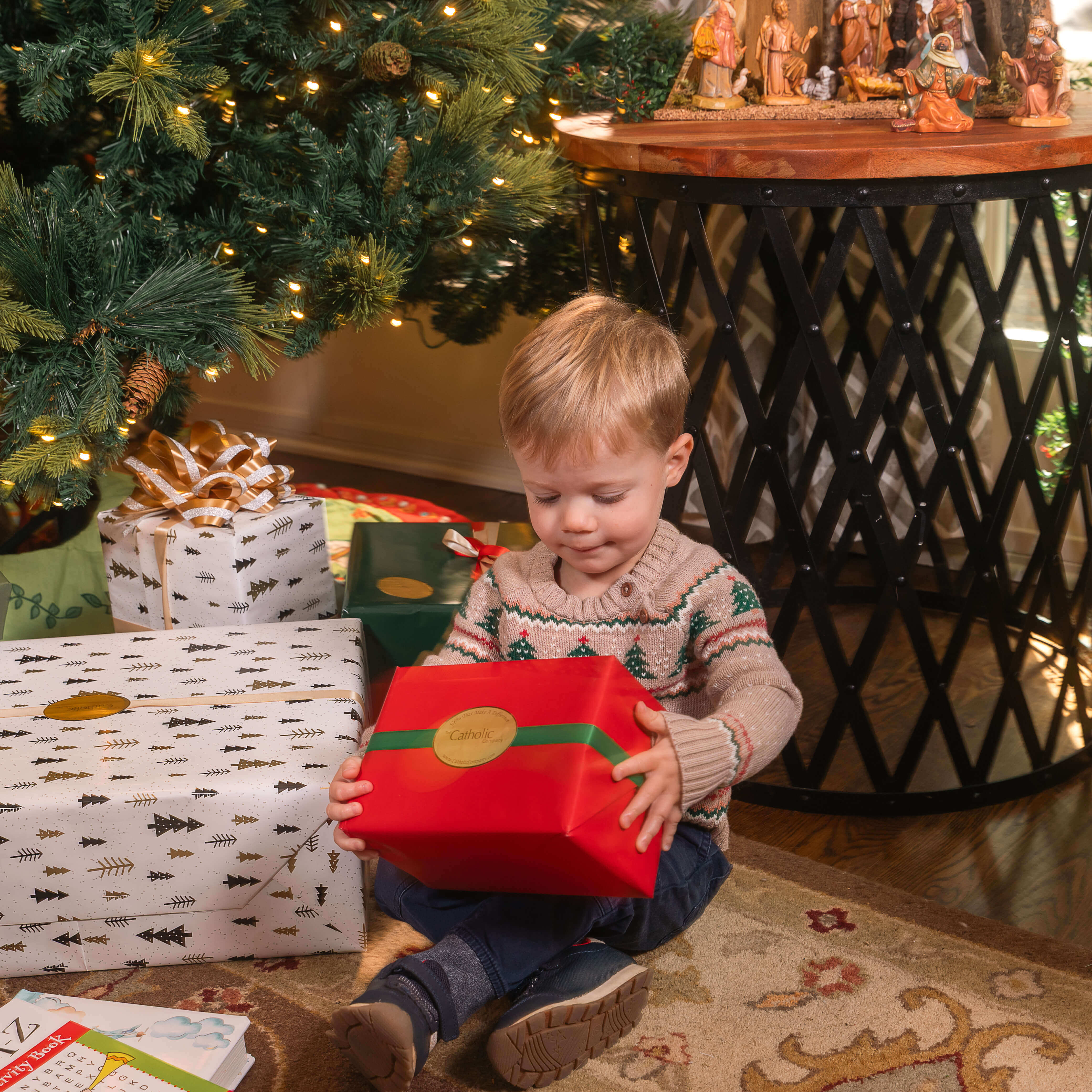 Young boy opening up wrapped Christmas gifts under a Christmas tree.