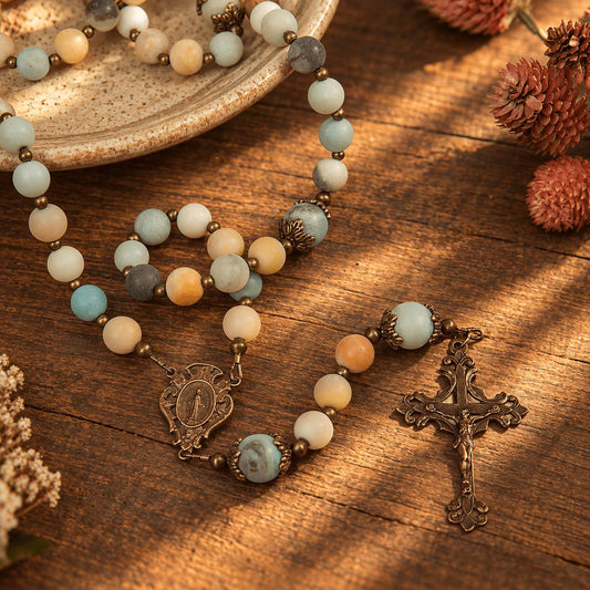 Blue and earth toned gem stone rosary with ornate crucifix and miraculous medal on a wood background.