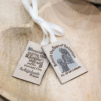 Two Scapulars with text and an illustration of a saint on a wooden surface.