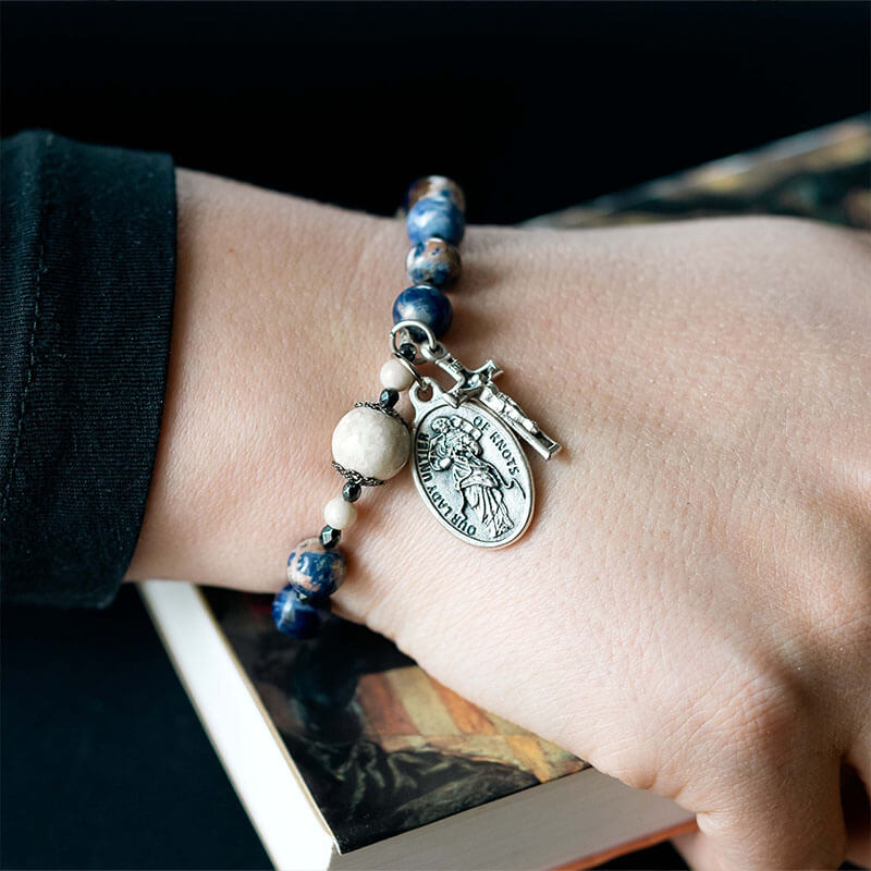 Close-up of a wrist wearing a beaded bracelet with a charm, against a dark background.