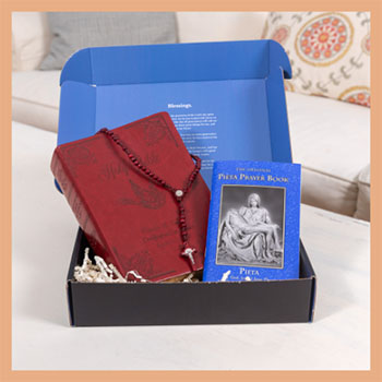 Red prayer book and blue Pieta Prayer Book in a box on a couch.