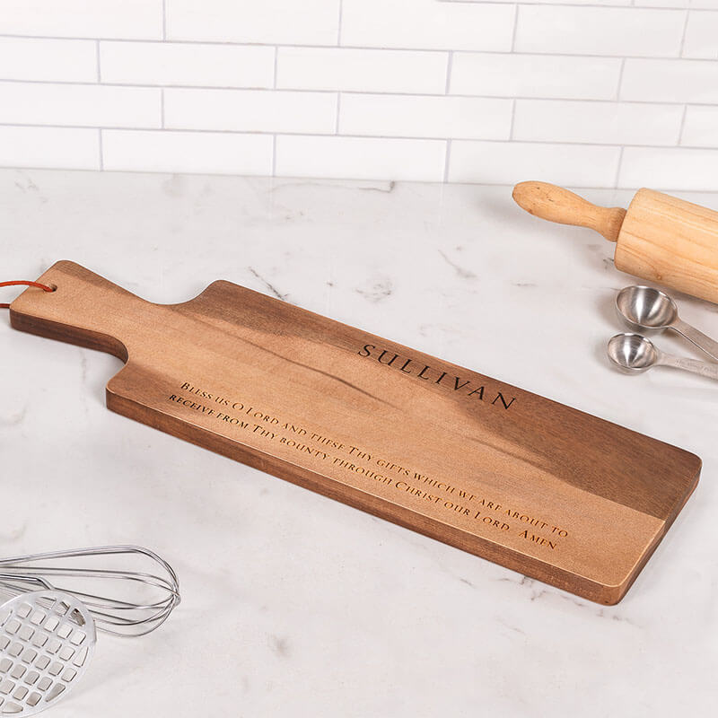 Wooden cutting board with engraved text on a marble countertop.