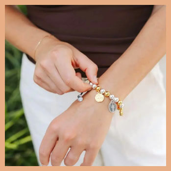 Person adjusting a bracelet with various charms on a blurred natural background