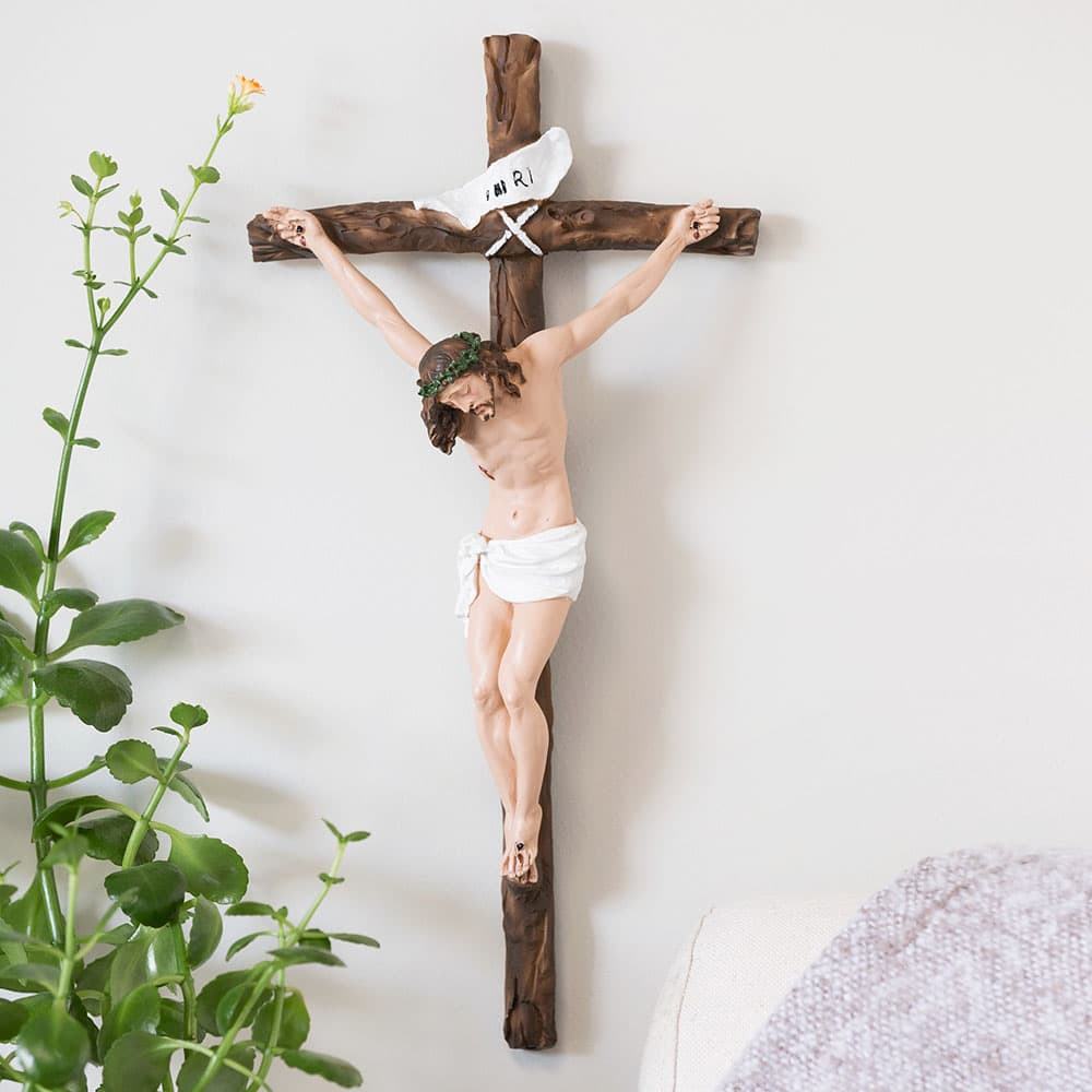 Wooden crucifix on a white wall, next to a plant.