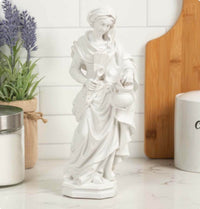 White ceramic statue of a woman holding a jar and spoon in a kitchen setting.