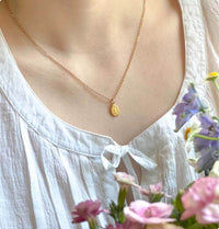 Woman wearing a gold necklace with flowers in the background