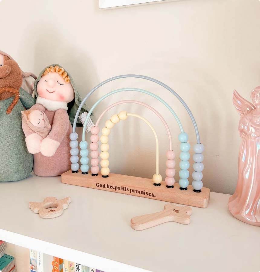 Colorful wooden rainbow toy on a shelf with soft toys and a quote plaque that says, 'God keeps His promises.'