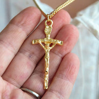 Gold crucifix pendant held in a hand against a neutral background