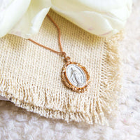 Gold necklace with a religious pendant on a textured beige surface