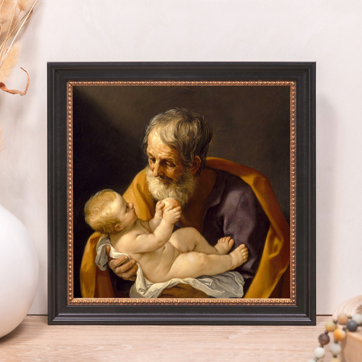 Framed painting of Saint Joseph and baby Jesus with black frame and gold beading.