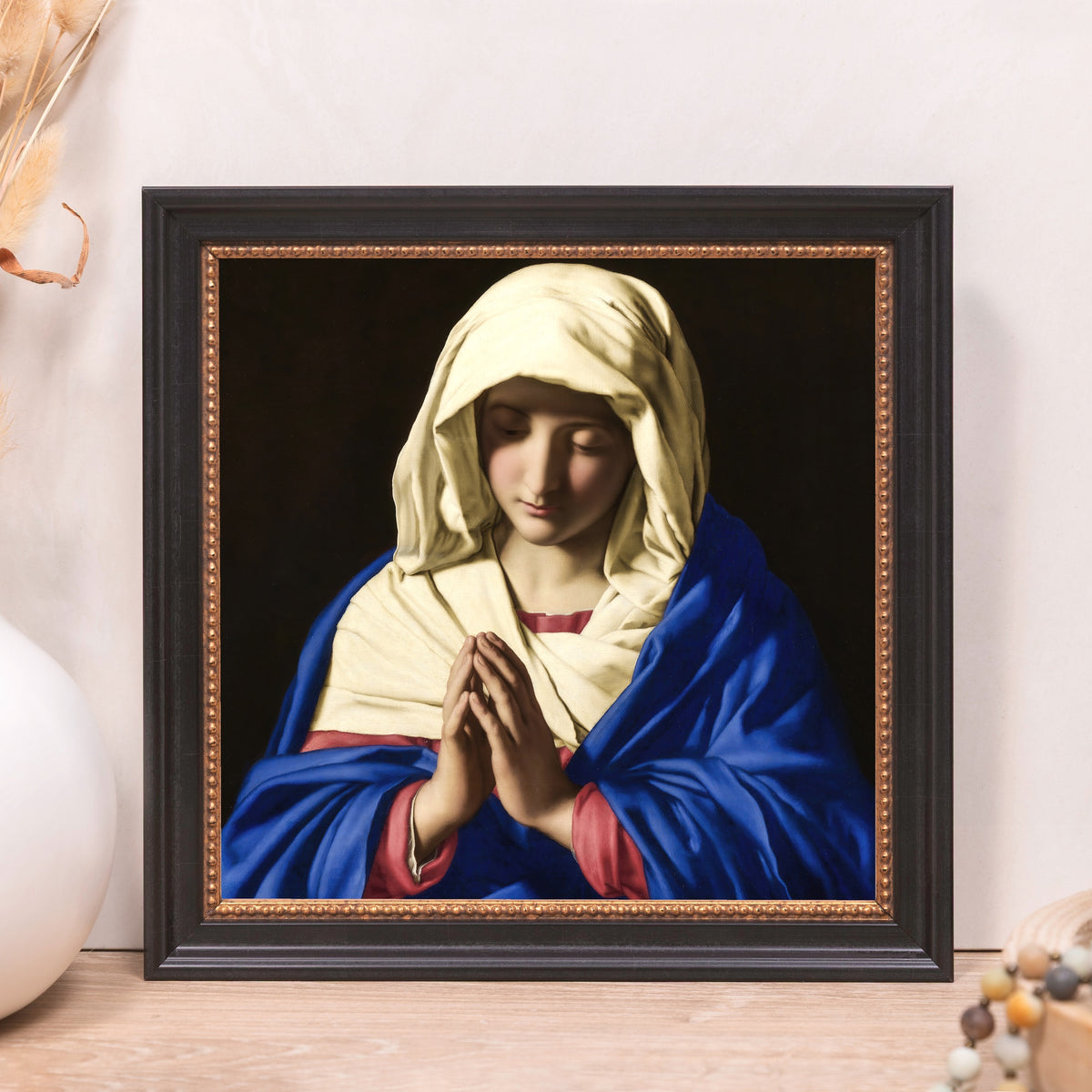 Framed painting of Mary in prayer, wearing a blue robe and head covering with a black background.