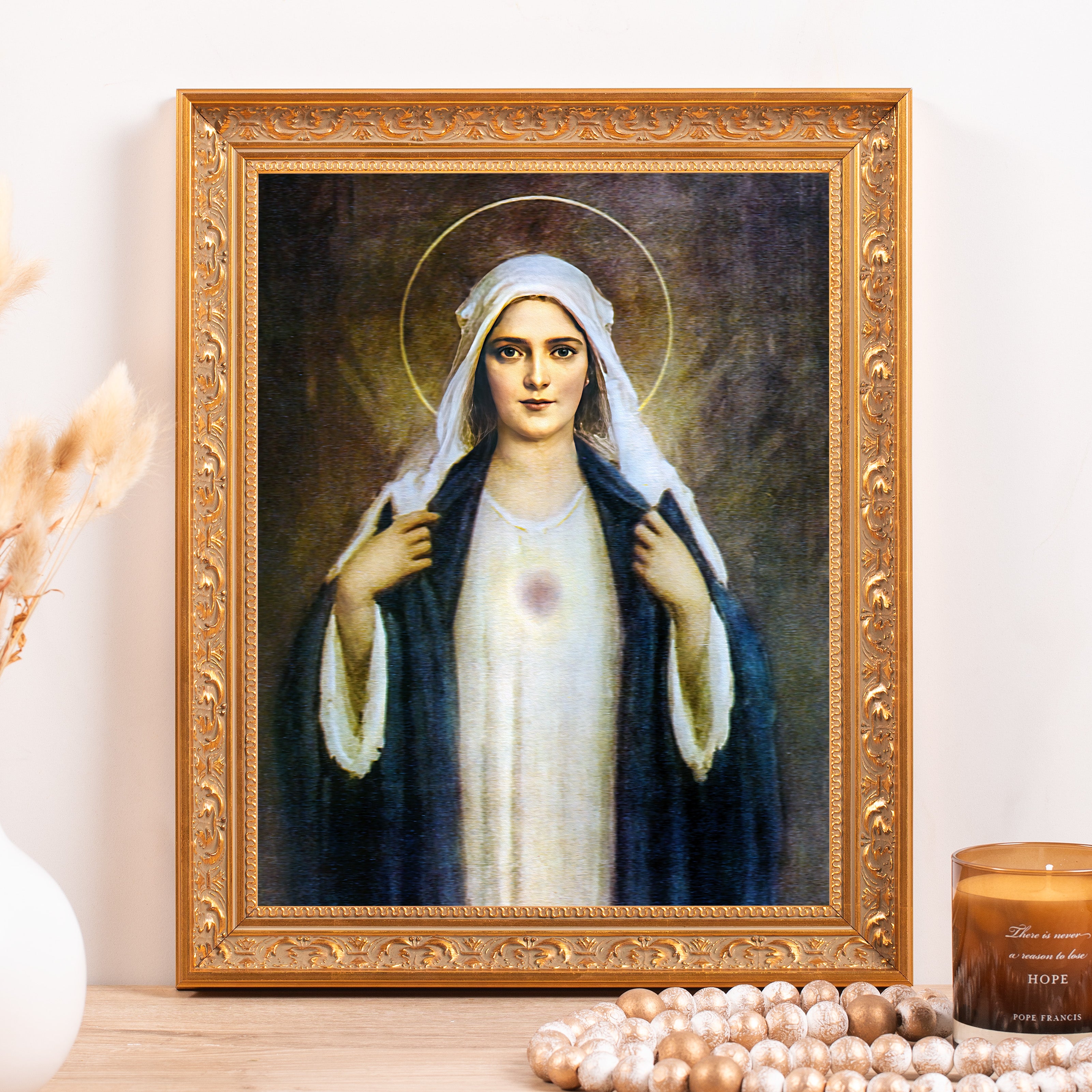 Framed portrait of Our Lady of Grace; the figure wears a white dress and blue cape in an ornate gold frame.