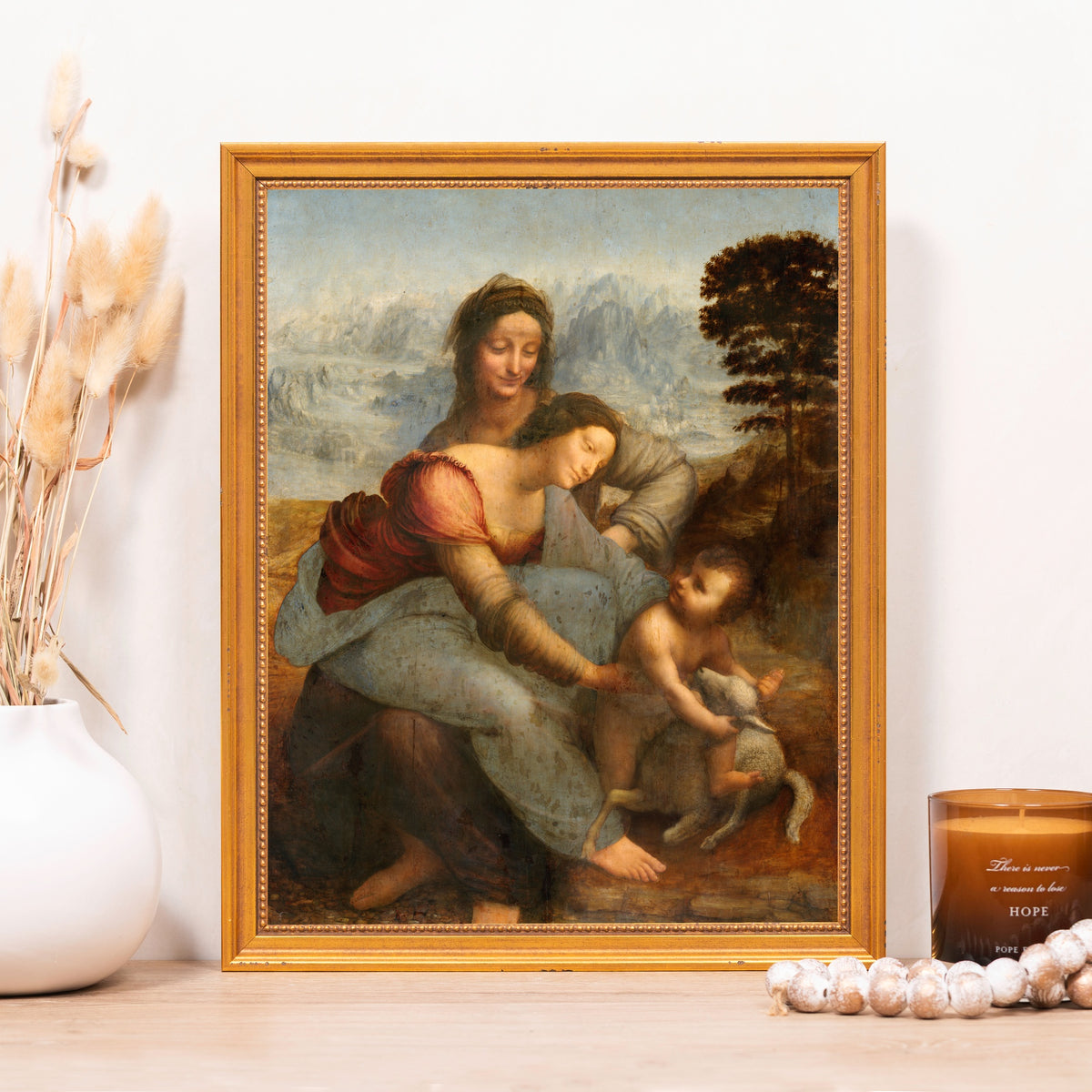 Framed print of Leonardo da Vinci's "The Virgin and Child with Saint Anne" in a gold frame, showing 3 people in reds and blues.