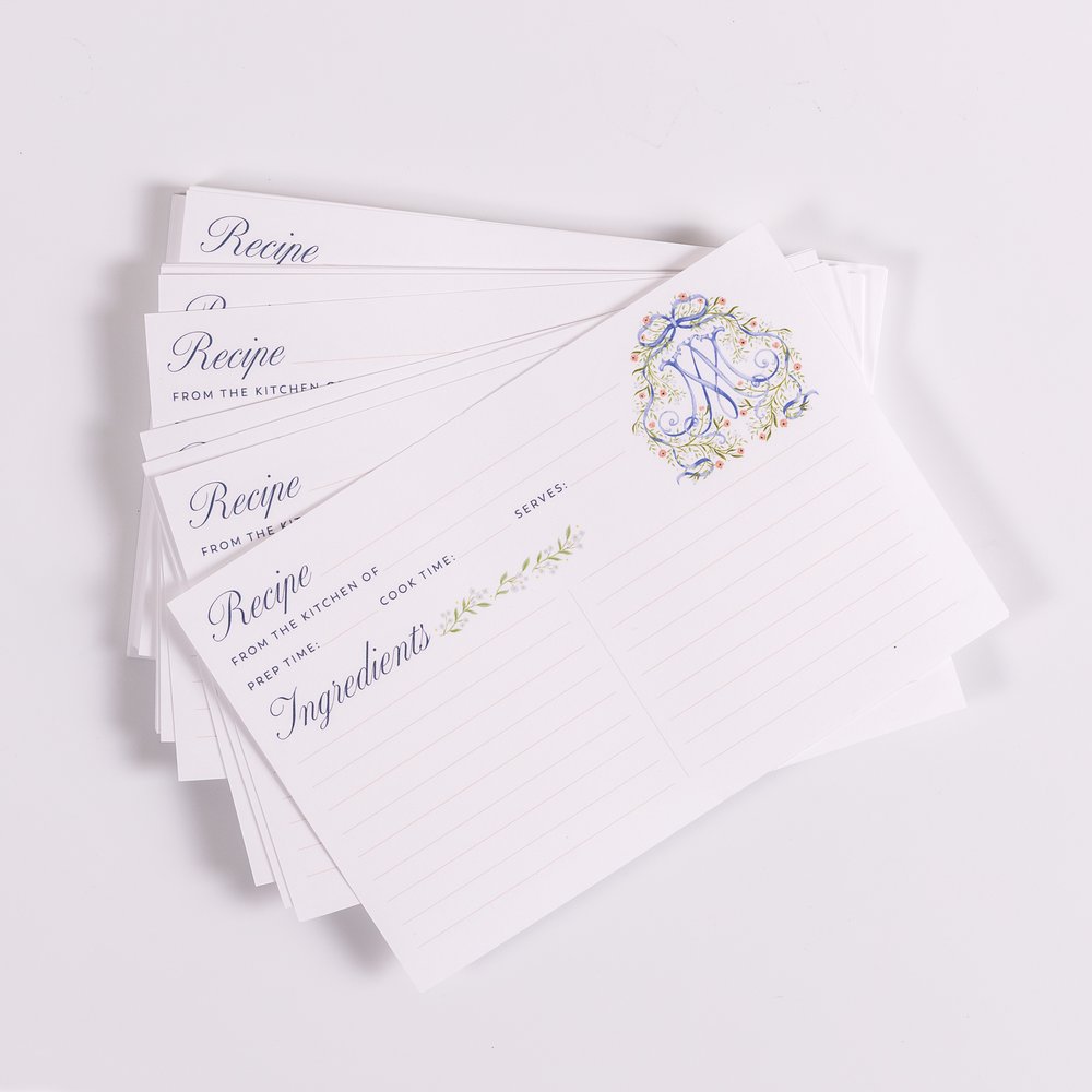 Stack of white recipe cards with lines and floral monogram design.