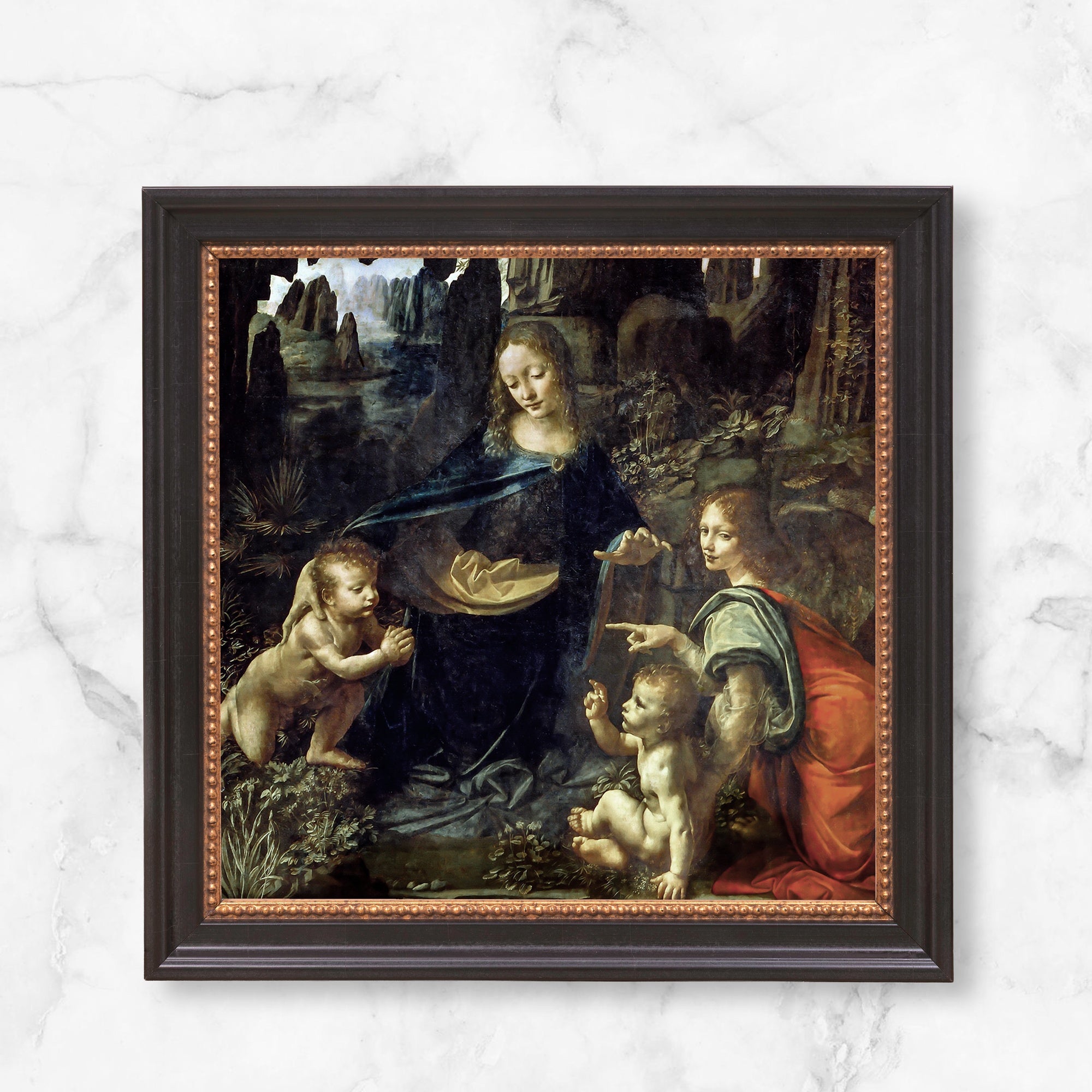 Framed painting of Virgin of the Rocks by Da Vinci, featuring figures in a dark, rocky landscape with a dark wood and gold frame.