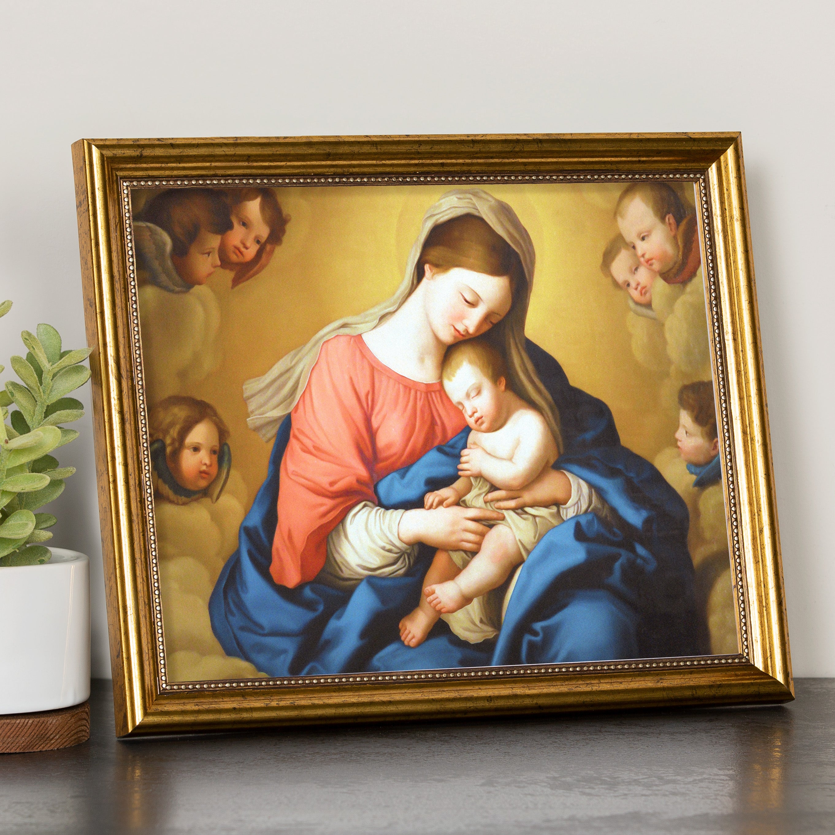 Framed religious print depicting Mary and baby Jesus surrounded by angels in soft hues, set in an ornate gold frame.