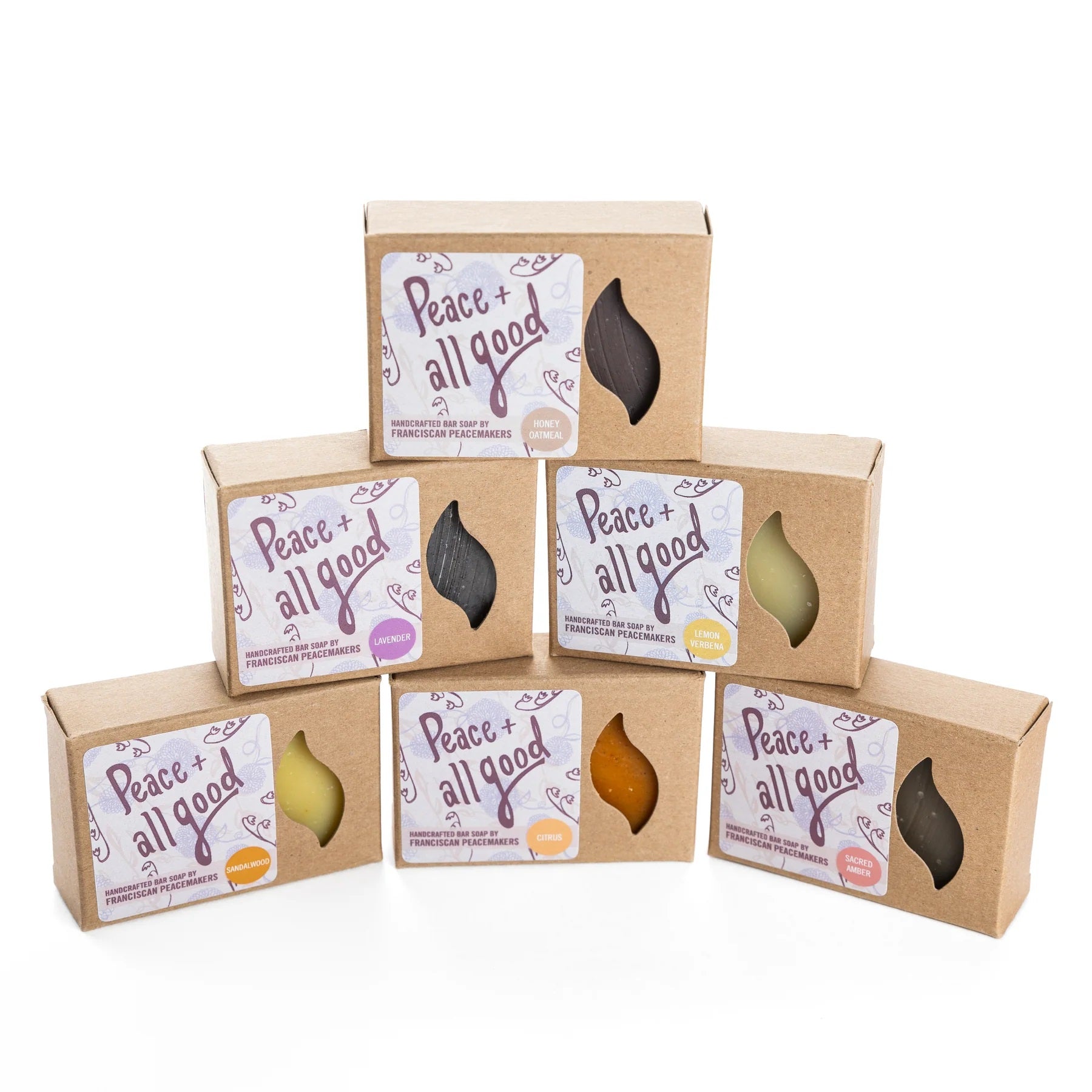 Assortment of artisan soaps in brown boxes with leaf-shaped windows showing various colors and scents.