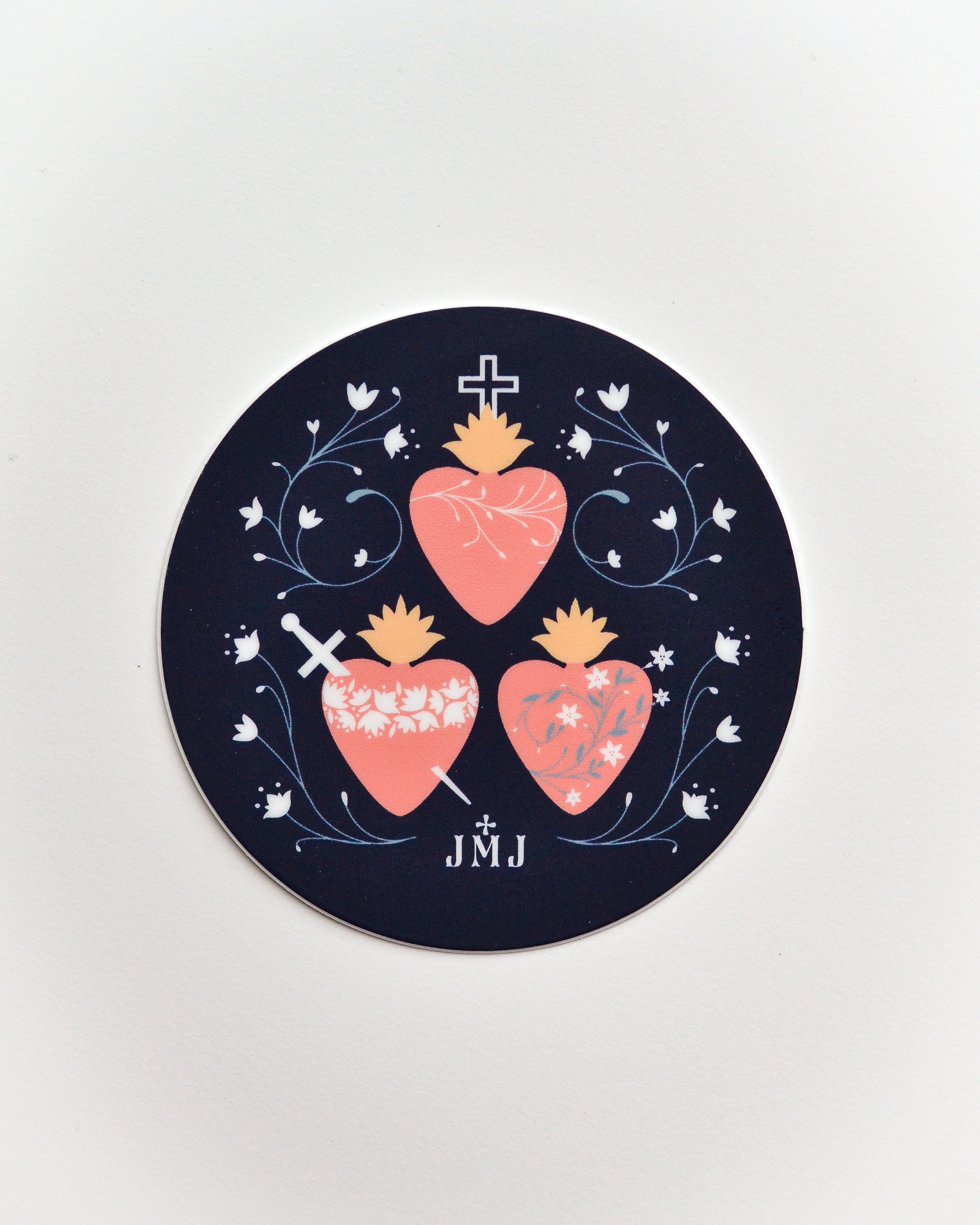 Circular sticker with a navy background, three pink hearts, floral designs, and religious symbolism.