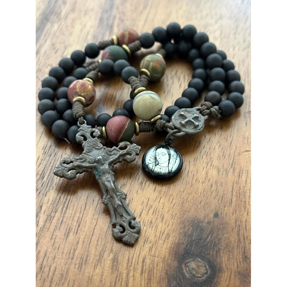 Catholic rosary made of black beads with metal crucifix and pendant on brown wood surface.