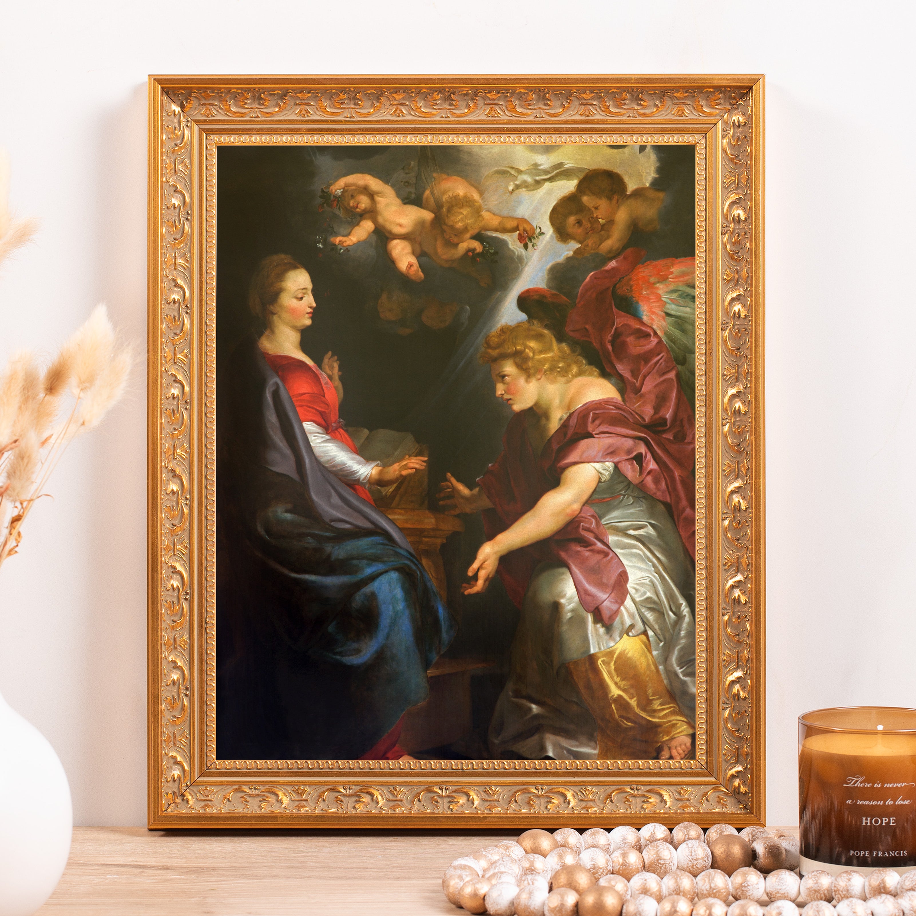 Framed reproduction art print of "The Annunciation" in an ornate gold frame, displayed on a wood surface.
