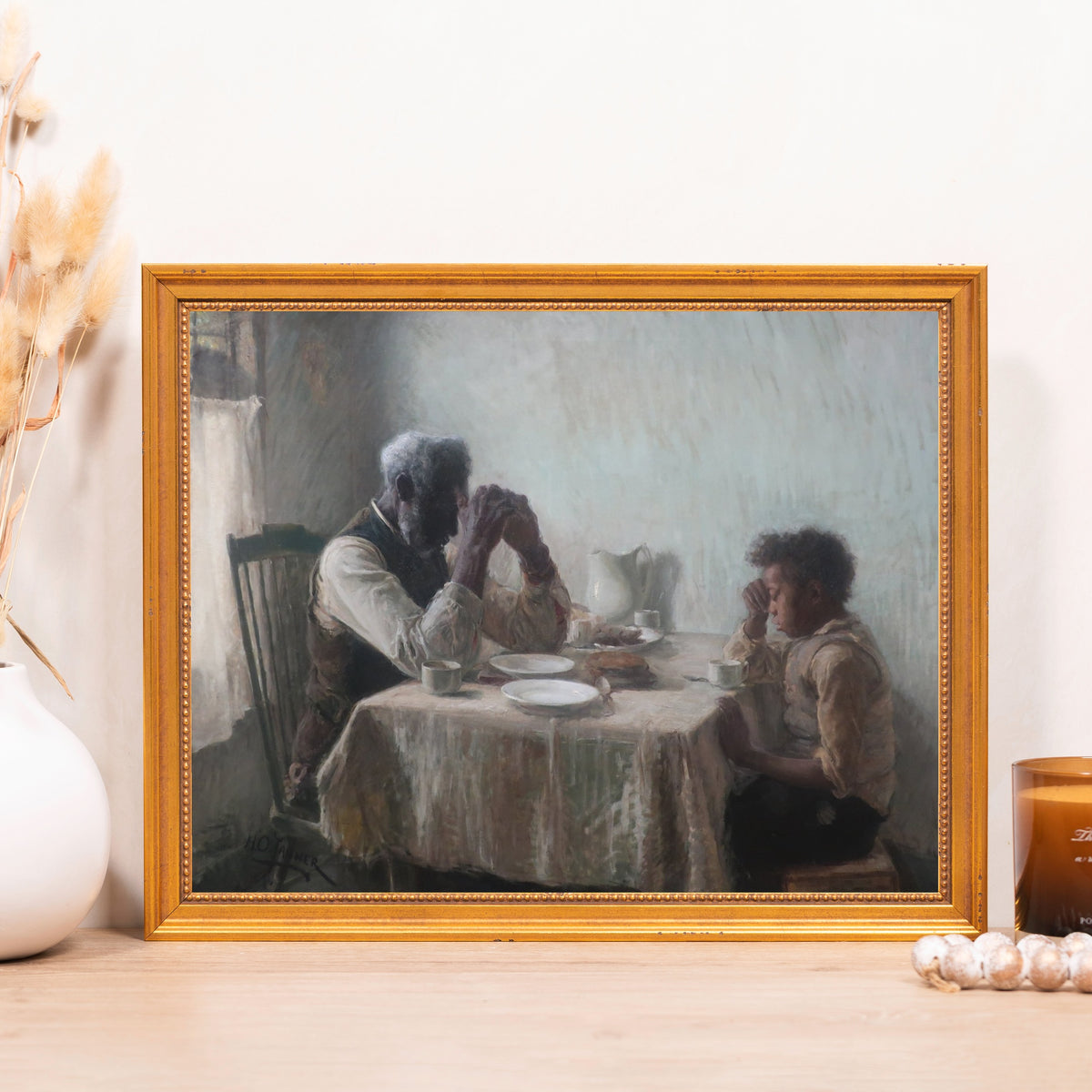 Framed painting shows an older man and boy praying before eating a meal in muted tones.