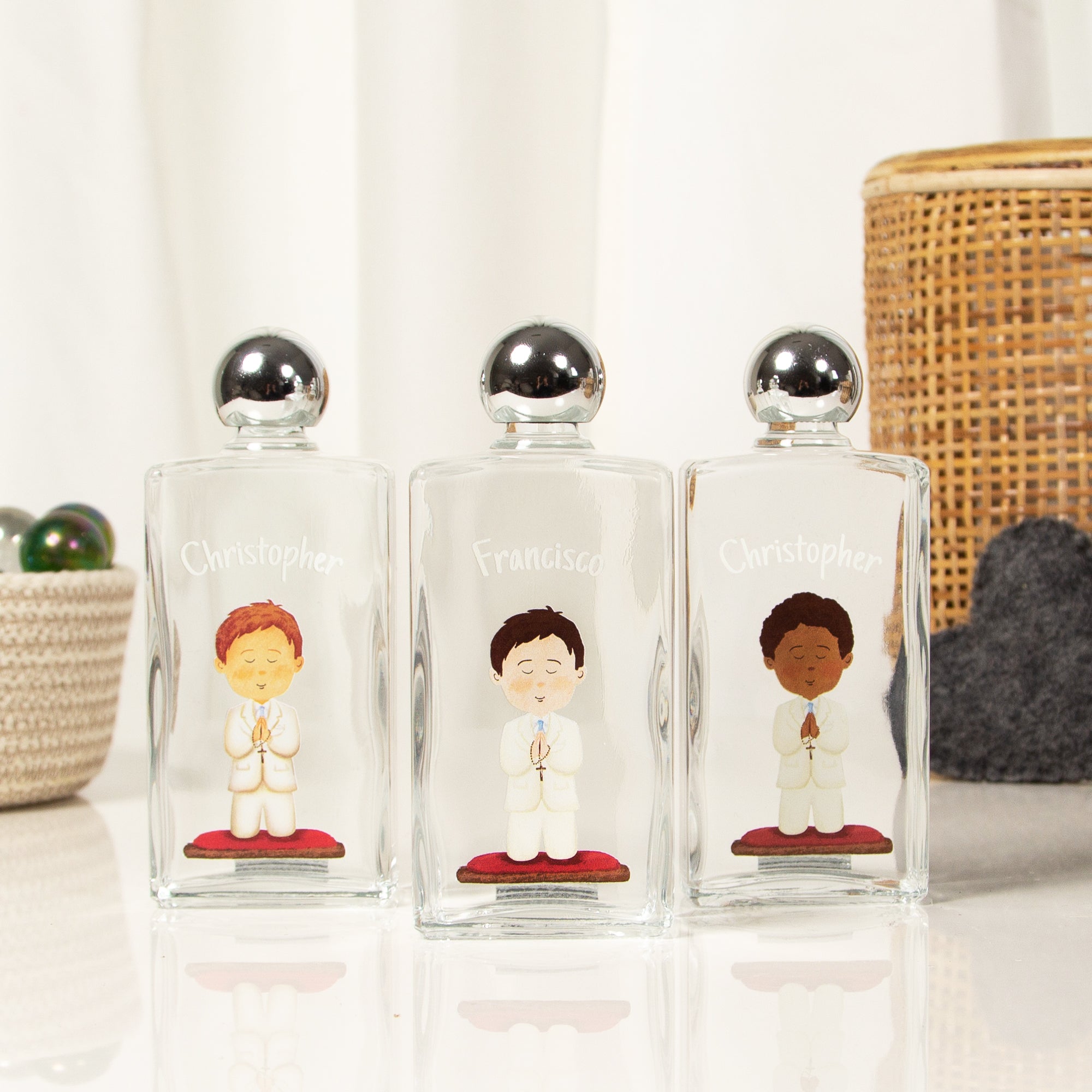 Personalized, clear glass baptism favors with silver lids and illustrations of praying boys on red cushions.