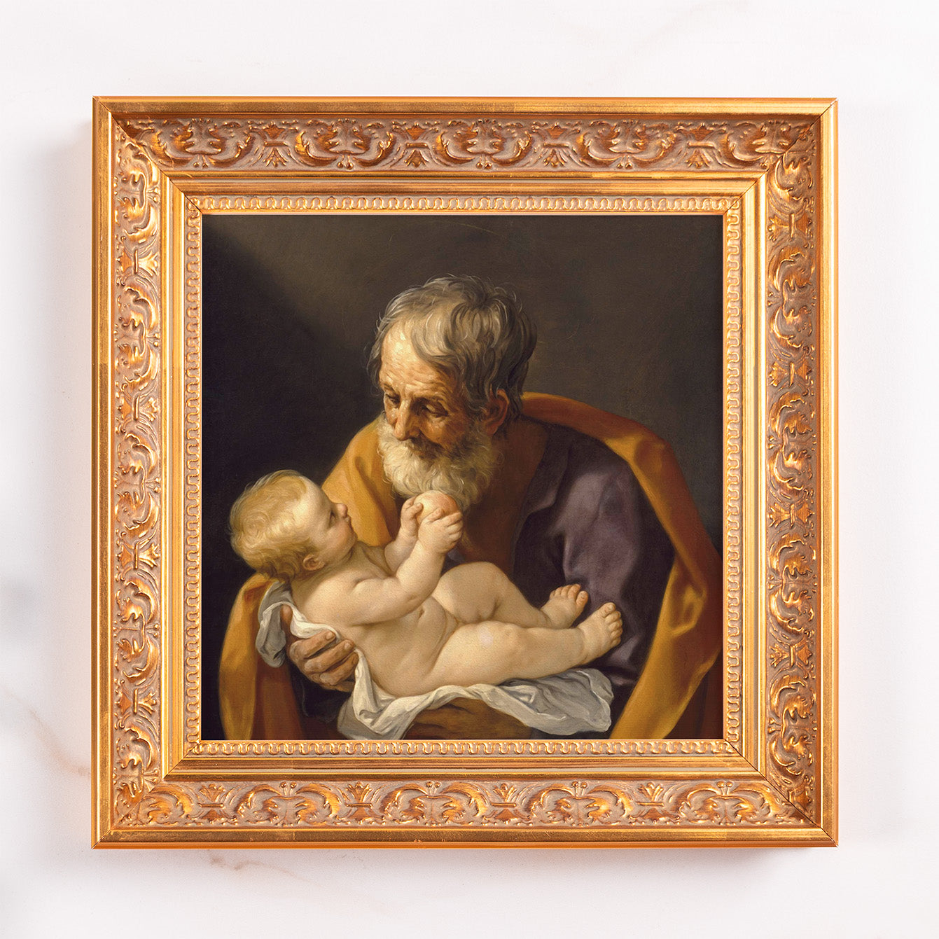 Framed painting depicting Saint Joseph holding baby Jesus in a gold ornate frame.
