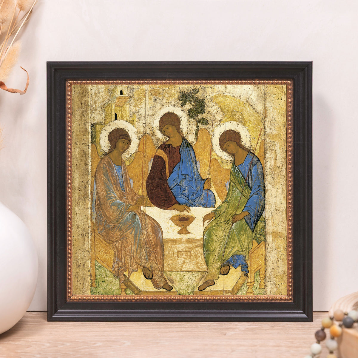Framed icon print depicting three haloed figures in blue, brown, and green robes sitting around a table.