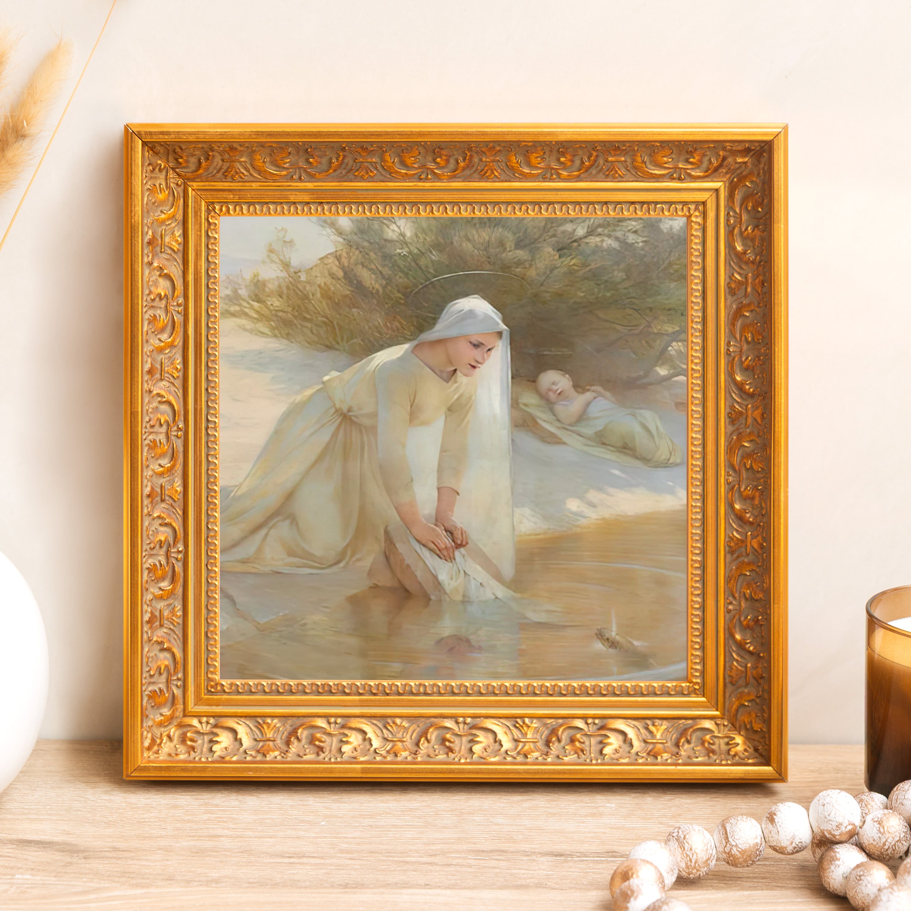 Framed art print depicting a woman washing clothes in the water, in a gold ornate frame.