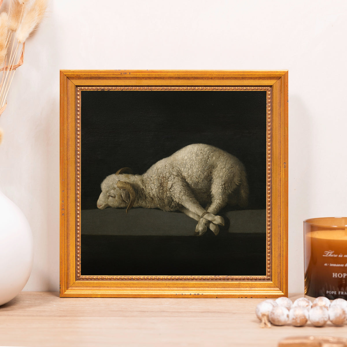 Framed print of a sleeping white sheep with bound legs in a gold frame.