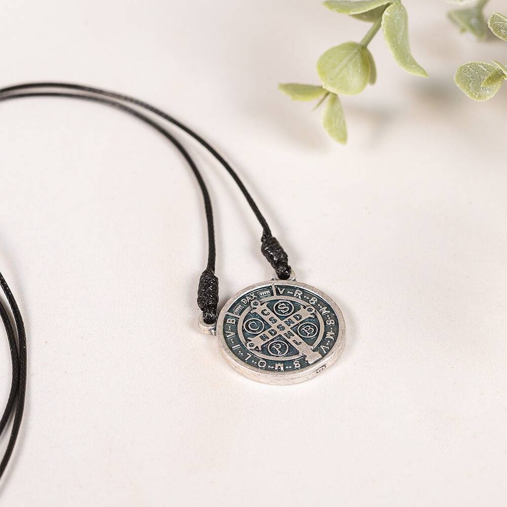St. Benedict medal necklace with a round silver pendant and black cord.