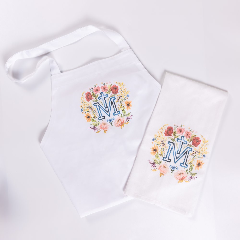White apron and dish towel set with "M" monogram and floral wreath design.