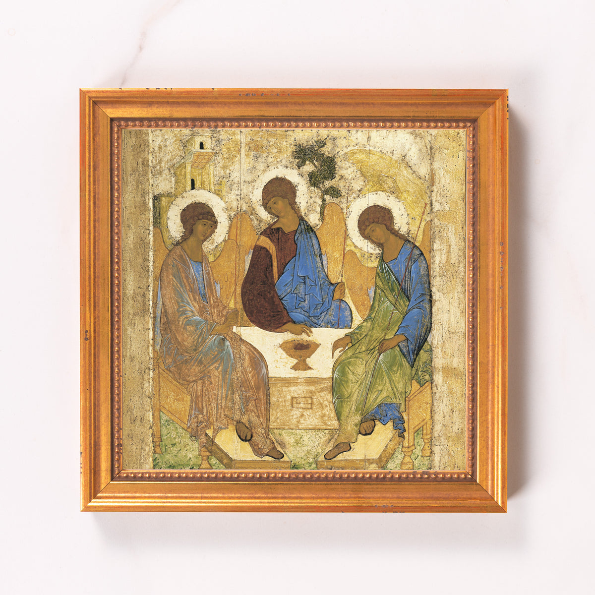 Framed painting depicts three figures with halos in blue and brown robes around a table.