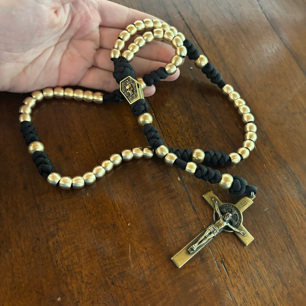 Religious rosary of gold beads and black cording with a gold cross and coffin-shaped pendant on wood surface.