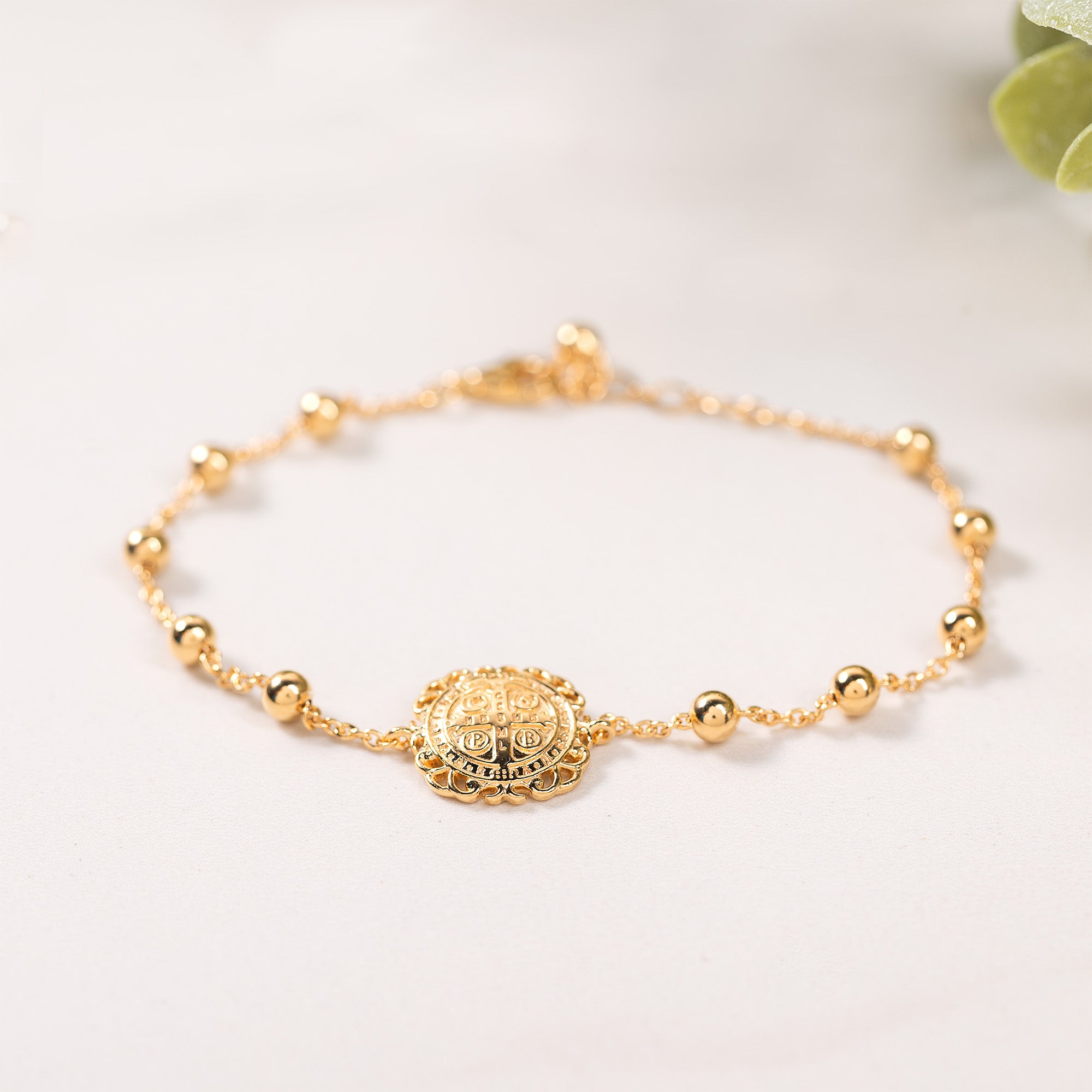 Gold-tone St. Benedict rosary bracelet with small beads and an ornate medallion charm on a delicate chain.